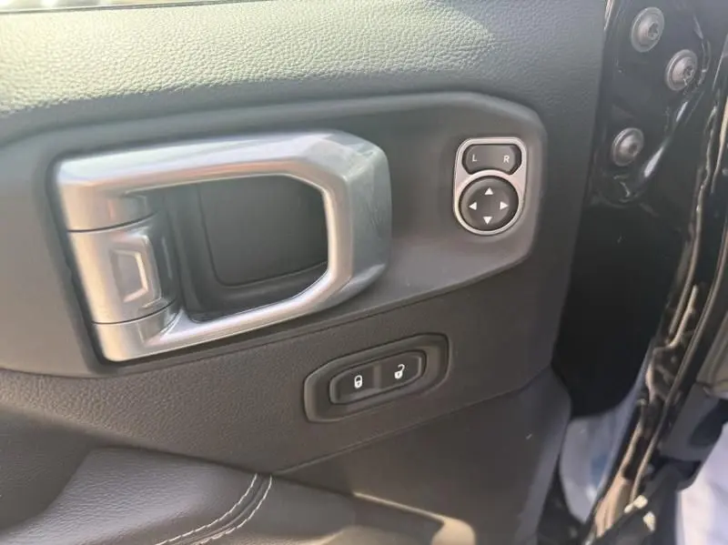 Gros plan sur la poignée intérieure et les commandes de réglage des rétroviseurs du côté gauche d’un Jeep Wrangler Unlimited noir 2022.