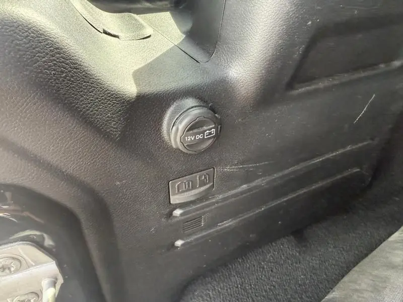 Détail intérieur montrant une prise 12V et un bouton de déverrouillage sur le côté droit du Jeep Wrangler Sahara noir 2022.