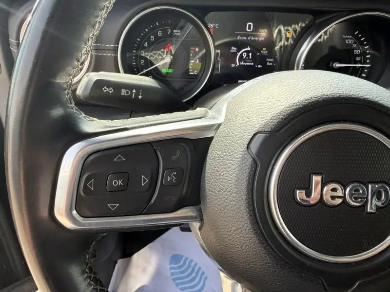 Vue rapprochée du volant noir de la Jeep Wrangler 2022 avec commandes intégrées et tableau de bord numérique.