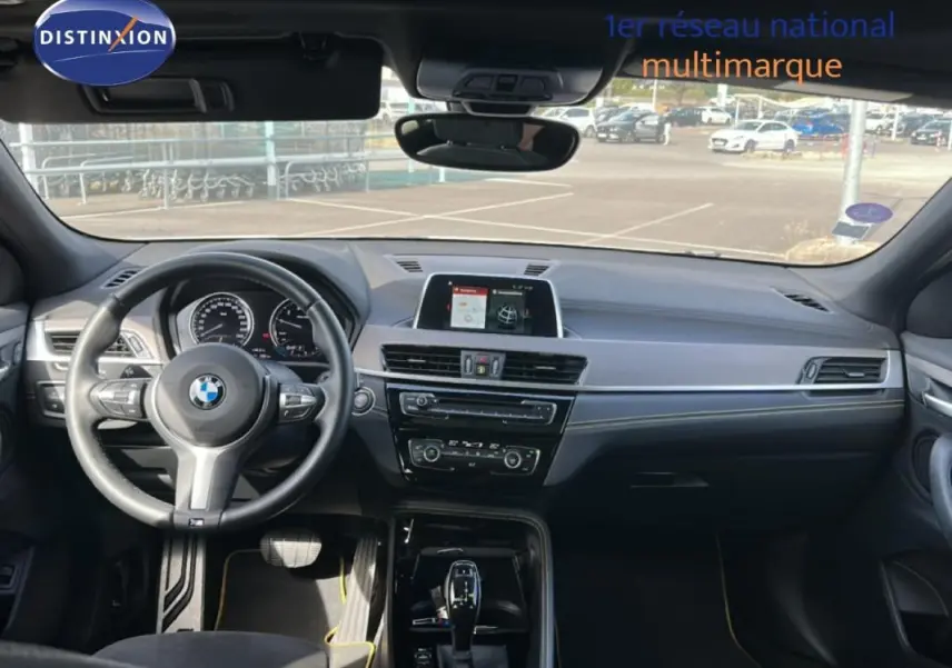 Vue intérieure avant du BMW X2 blanc 2018, volant sport, écran GPS central et tableau de bord moderne.