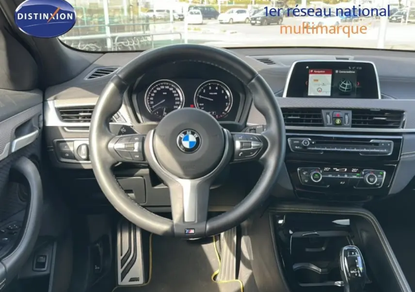 Vue intérieure centrée sur le volant sport et tableau de bord du BMW X2 blanc avec écran GPS et console noire brillante.