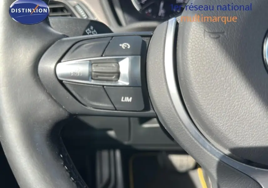 Gros plan sur le volant sport noir de la BMW X2 blanc, montrant les commandes de régulateur de vitesse côté gauche.