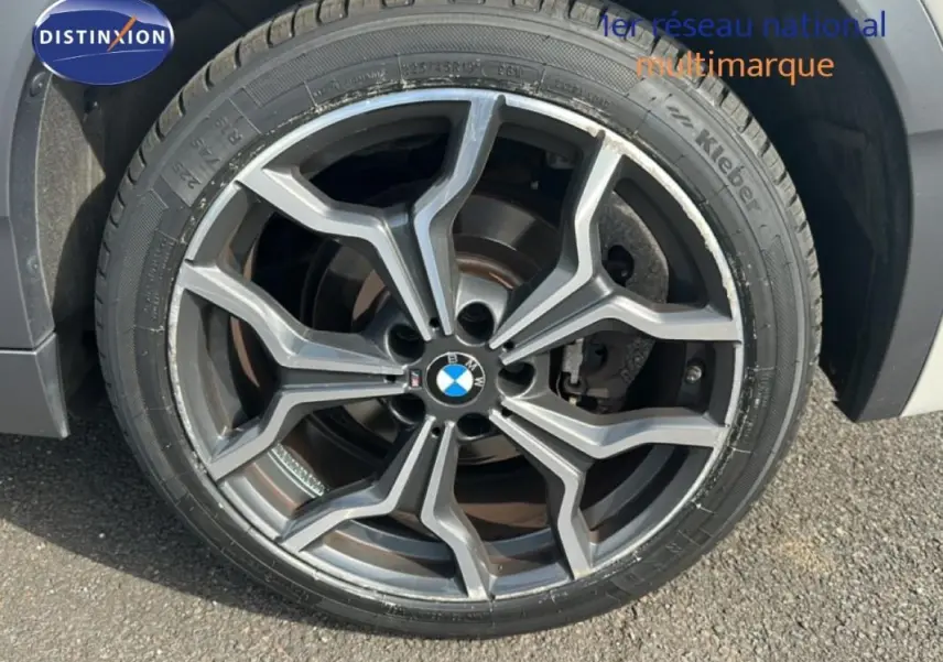 Gros plan sur la jante alliage 19 pouces gris foncé du BMW X2 blanc, mettant en valeur le logo central BMW.