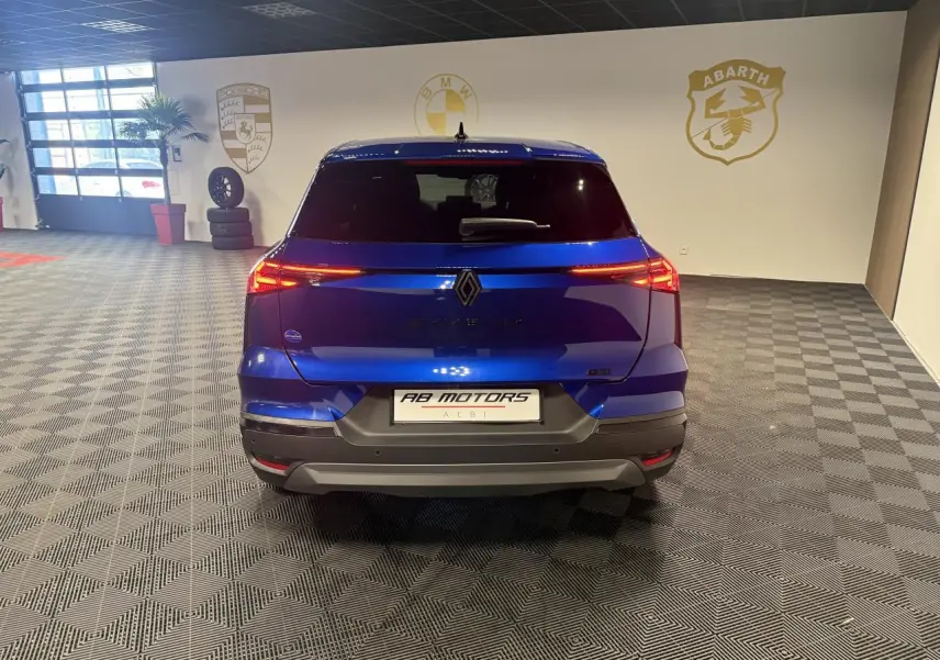 Vue arrière d'un Renault Symbioz bleu Iron 2025 avec feux LED allumés et logo Alpine dans un showroom.