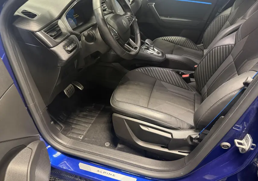 Intérieur côté conducteur de la Renault Symbioz bleu, sièges noirs avec surpiqûres bleues et seuil de porte Alpine visible.