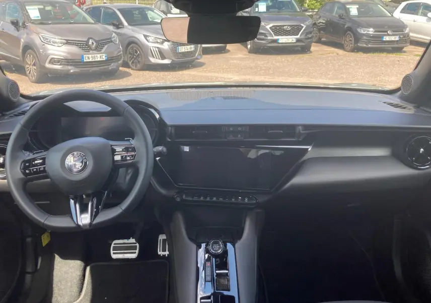 Vue intérieure avant de l'Alfa Romeo Junior 1.2 hybride 2026, tableau de bord noir avec écran tactile et volant multifonction.