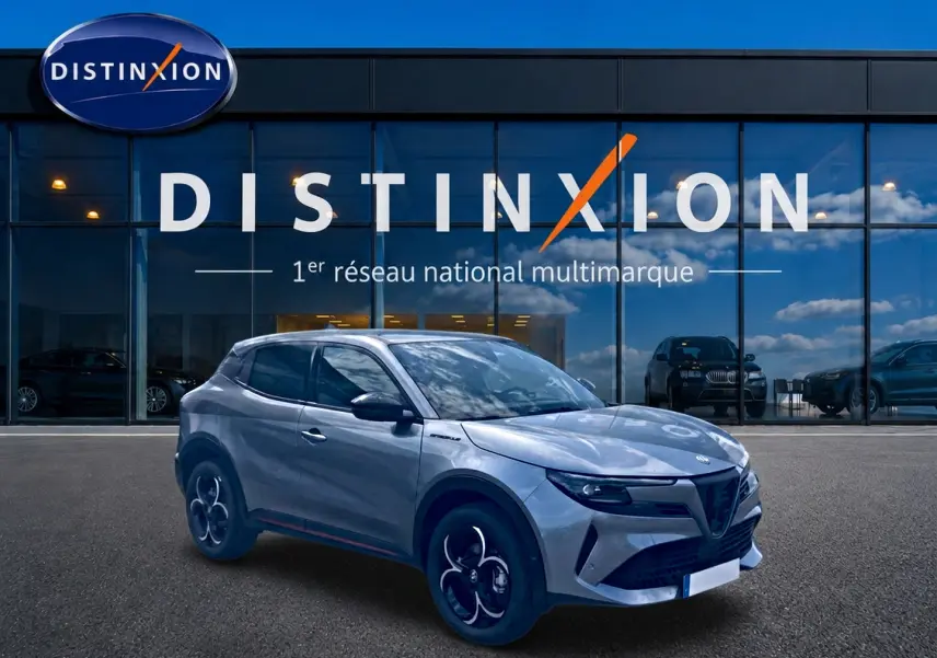 Vue 3/4 avant droite d'une Alfa Romeo Junior gris métallisé devant une vitrine Distinxion, avec jantes en alliage noires et détails noirs.