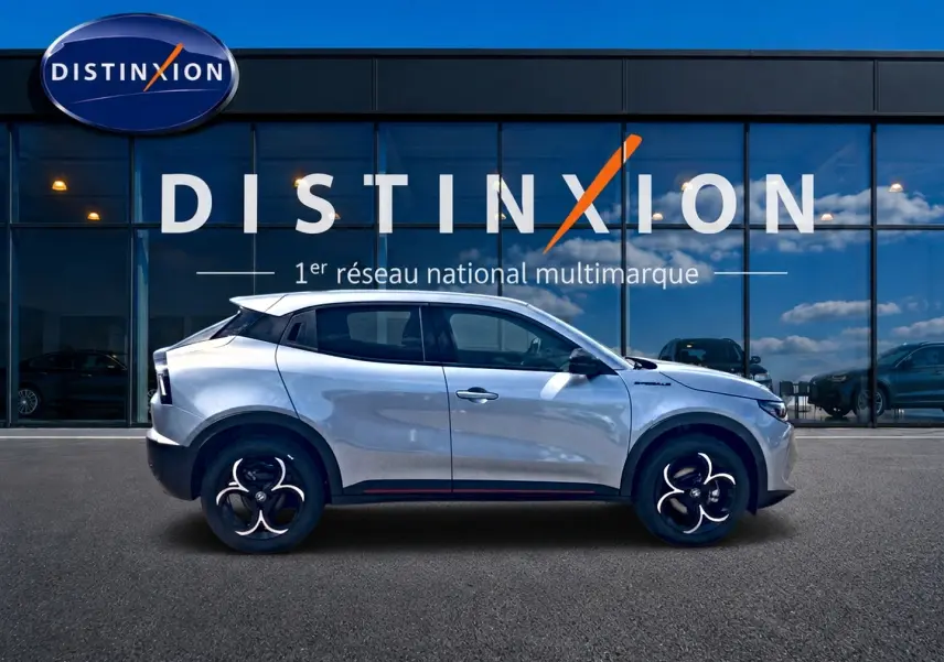 Vue de profil droit de l'Alfa Romeo Junior 1.2 hybride gris avec jantes en alliage devant une vitrine Distinxion.