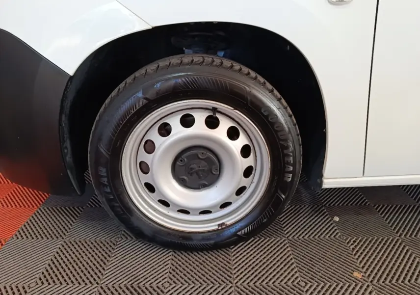 Gros plan sur la roue avant droite en jante acier du Peugeot Partner blanc, avec partie basse de la carrosserie visible.