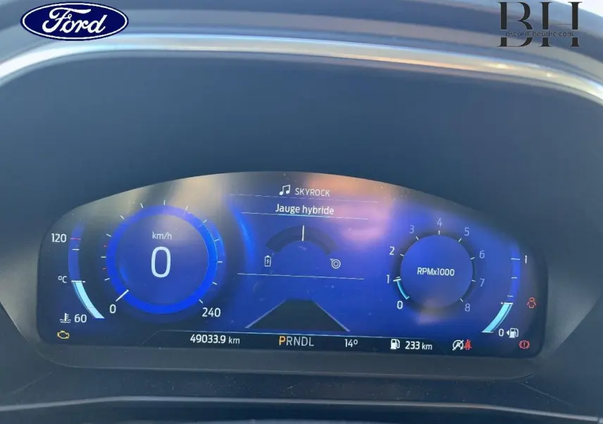 Tableau de bord numérique bleu de la Ford Focus 2023, affichant vitesse, régime et jauge hybride.