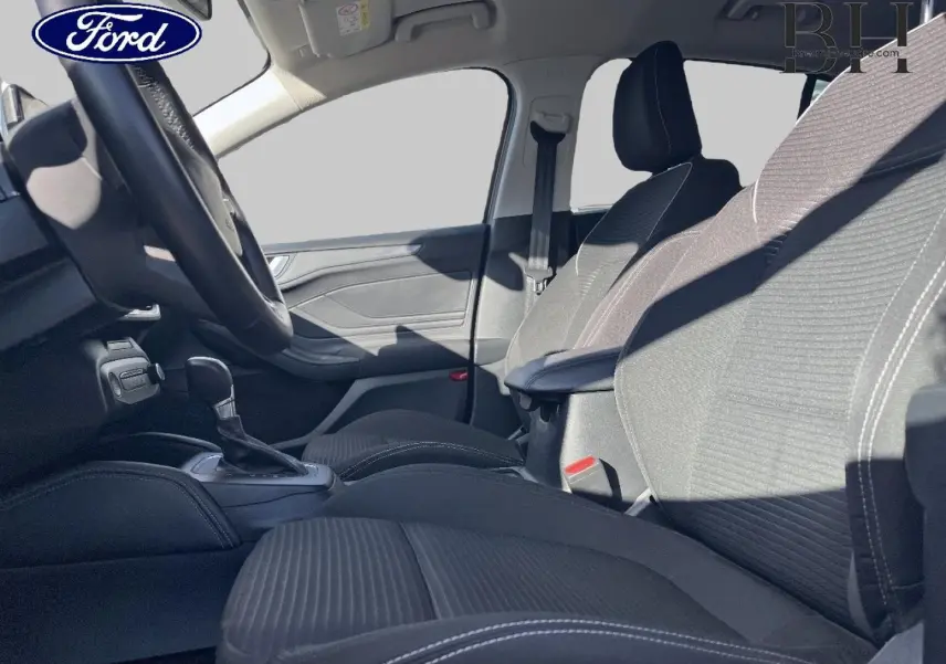 Vue intérieure côté conducteur de la Ford Focus 2023, sièges tissu noir avec surpiqûres blanches et accoudoir central.