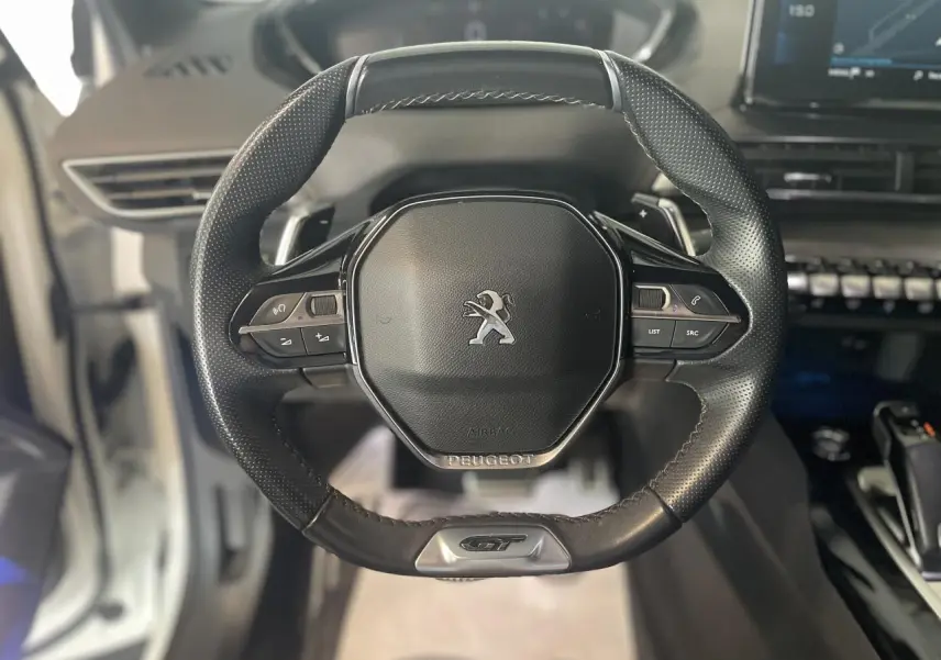 Gros plan sur le volant cuir perforé noir du Peugeot 3008 GT avec logo lion et badge GT en bas.