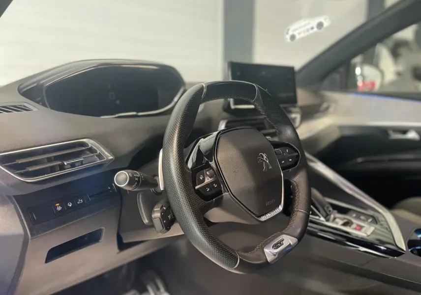 Vue intérieure centrée sur le volant GT cuir perforé et tableau de bord du Peugeot 3008 blanc nacré 2022.