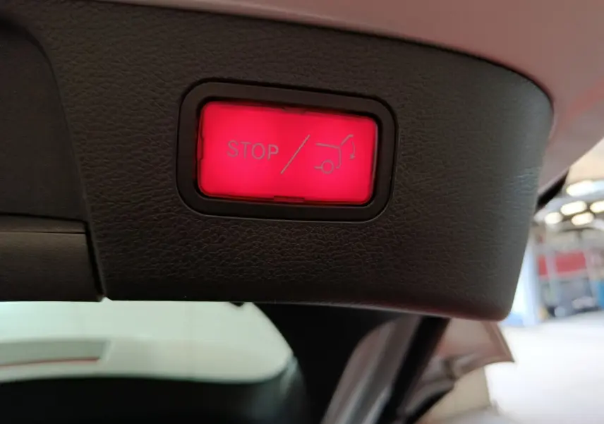 Bouton rouge d'arrêt électrique du coffre sur le hayon intérieur d'un Mercedes GLA gris clair, vue rapprochée.