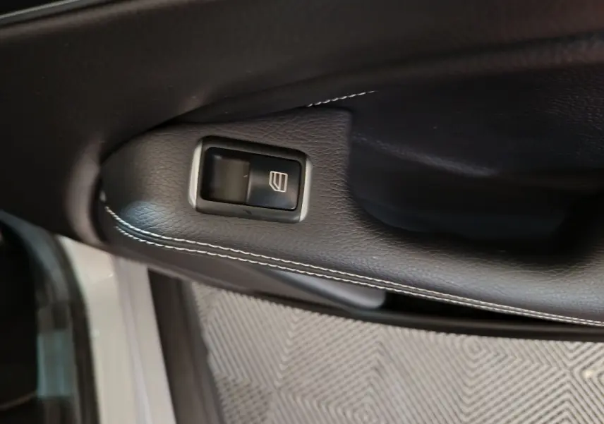 Gros plan sur le bouton de lève-vitre côté conducteur en cuir noir avec surpiqûres blanches, Mercedes GLA gris clair.