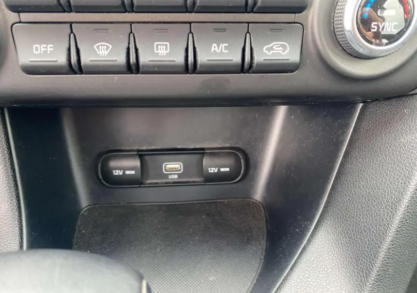 Détail de la console centrale avec commandes climatisation, prises 12V et port USB sur KIA Sportage gris foncé.