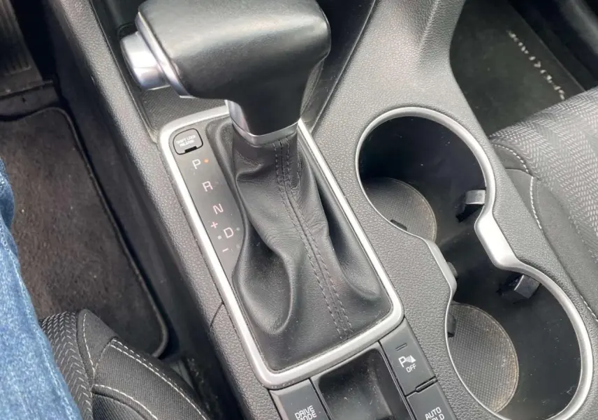 Gros plan sur la console centrale du Kia Sportage 2021, levier de vitesses cuir noir et porte-gobelets.