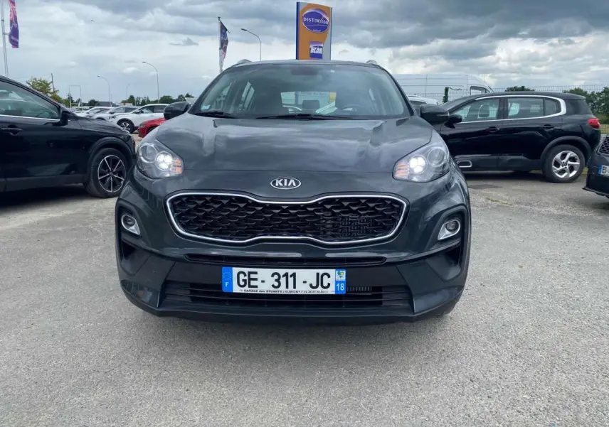 Vue de face du KIA Sportage gris foncé avec calandre noire et phares allumés sur un parking extérieur.