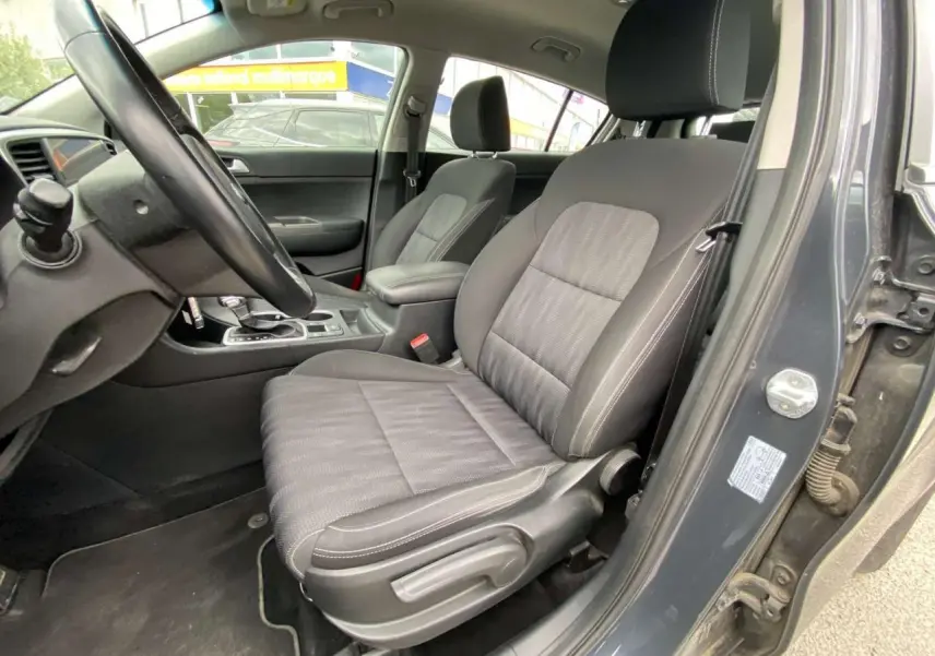 Vue intérieure côté conducteur du Kia Sportage gris foncé 2021, mettant en valeur le siège avant et le volant cuir.