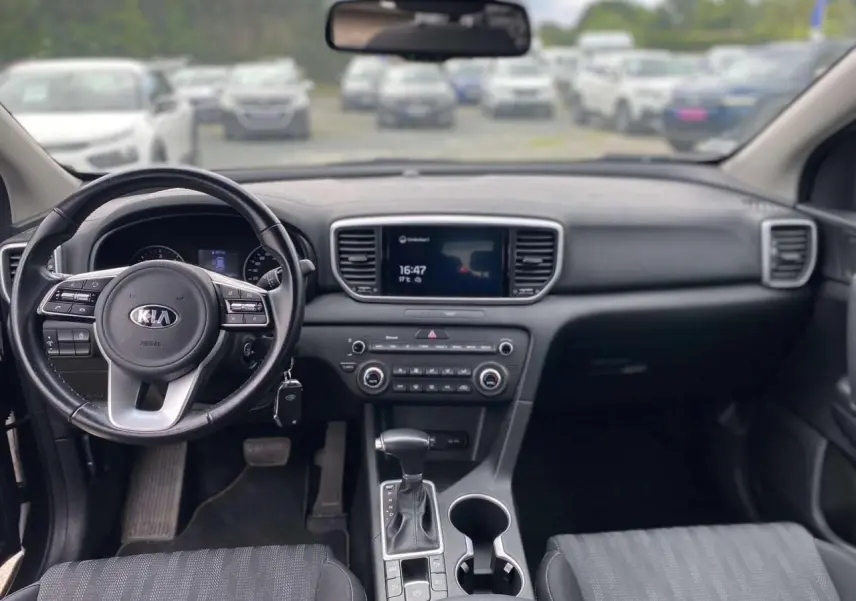 Vue intérieure avant du Kia Sportage 2021, tableau de bord noir avec volant cuir et écran tactile central.