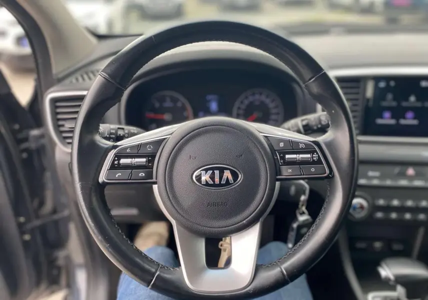 Vue centrée sur le volant cuir noir du Kia Sportage 2021, avec tableau de bord et écran tactile en arrière-plan flou.
