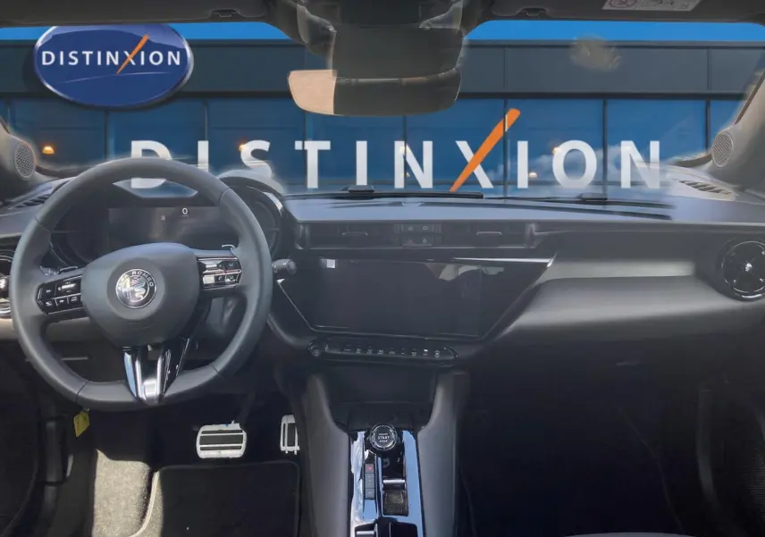 Vue intérieure frontale de l'Alfa Romeo Junior 1.2 hybride 2026, tableau de bord noir avec écran tactile et volant multifonction.