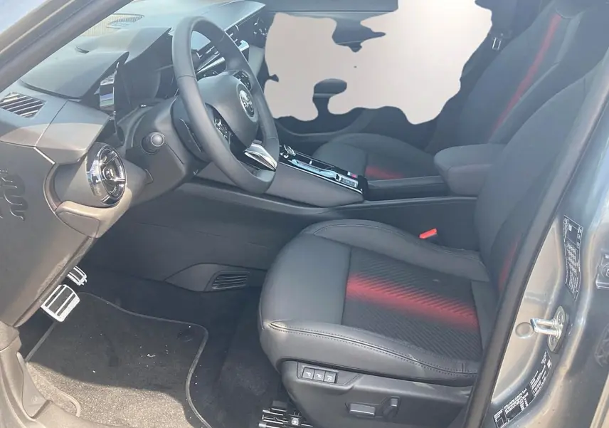 Vue intérieure côté conducteur de l'Alfa Romeo Junior 1.2 hybride grise, sièges noirs avec surpiqûres rouges et volant multifonction.