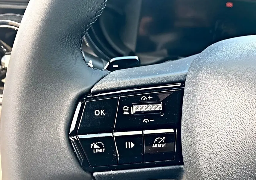 Gros plan sur les commandes noires au volant gris de l'Alfa Romeo Junior 1.2 hybride 2026, avec boutons de régulateur et assistance.