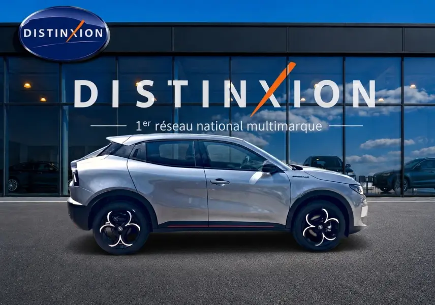 Vue de profil côté gauche d'une Alfa Romeo Junior grise garée devant une vitrine avec logo Distinxion.