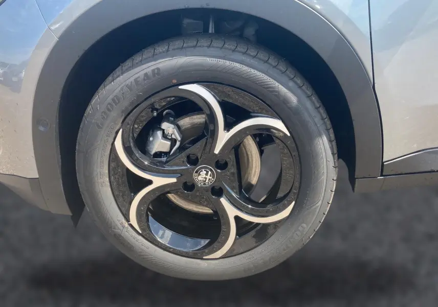 Gros plan sur la roue avant droite grise d'une Alfa Romeo Junior 1.2 hybride avec jante alliage noire et argentée au design distinctif.