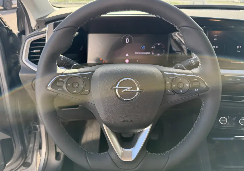 Volant en cuir noir de l'Opel Grandland 2024, avec commandes intégrées et tableau de bord numérique en arrière-plan.