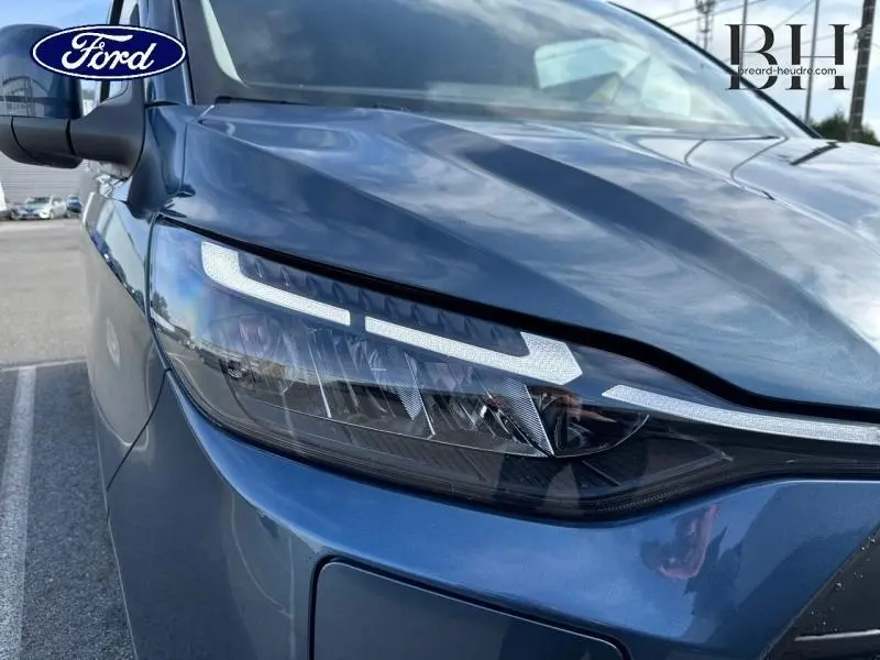 Gros plan sur le phare avant gauche du Ford Transit Custom Fourgon bleu azur métallisé, soulignant ses lignes modernes.