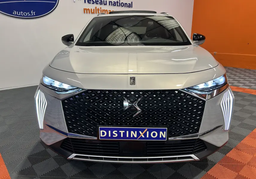 Vue frontale du DS7 BlueHDI 130 en Chrystal pearl avec calandre noire et phares LED allumés en intérieur showroom.