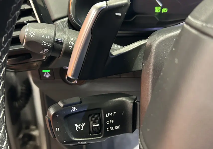 Gros plan sur les commandes du régulateur de vitesse à gauche du volant du DS7 2024 couleur Chrystal pearl.