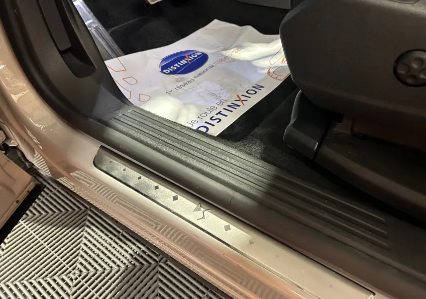 Vue rapprochée de la porte côté gauche du DS7 Chrystal pearl, montrant la plaque de seuil avec logo DS et tapis intérieur noir.