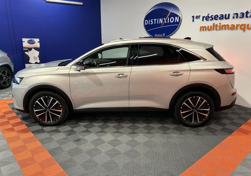 Vue latérale droite du DS7 BlueHDI 130 en couleur Chrystal pearl, avec jantes noires et toit ouvrant visible en intérieur showroom.
