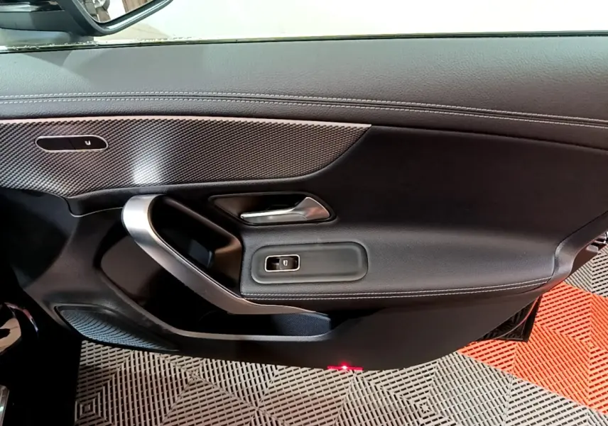 Vue intérieure côté gauche de la porte avant d’une Mercedes Classe A noire, avec garniture cuir et inserts argentés.