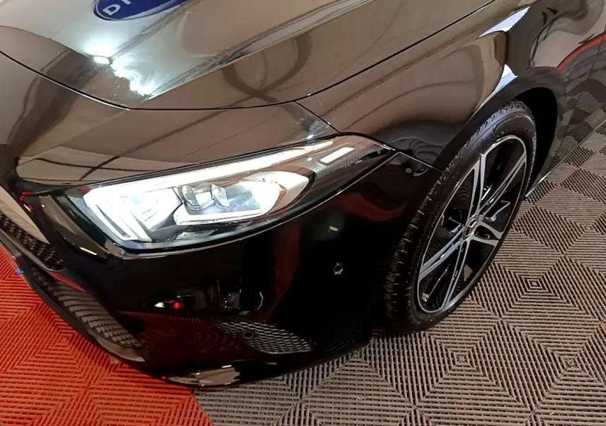 Gros plan sur l'avant droit noir brillant d'une Mercedes Classe A Berline 2022 avec phares LED et jante alliage.