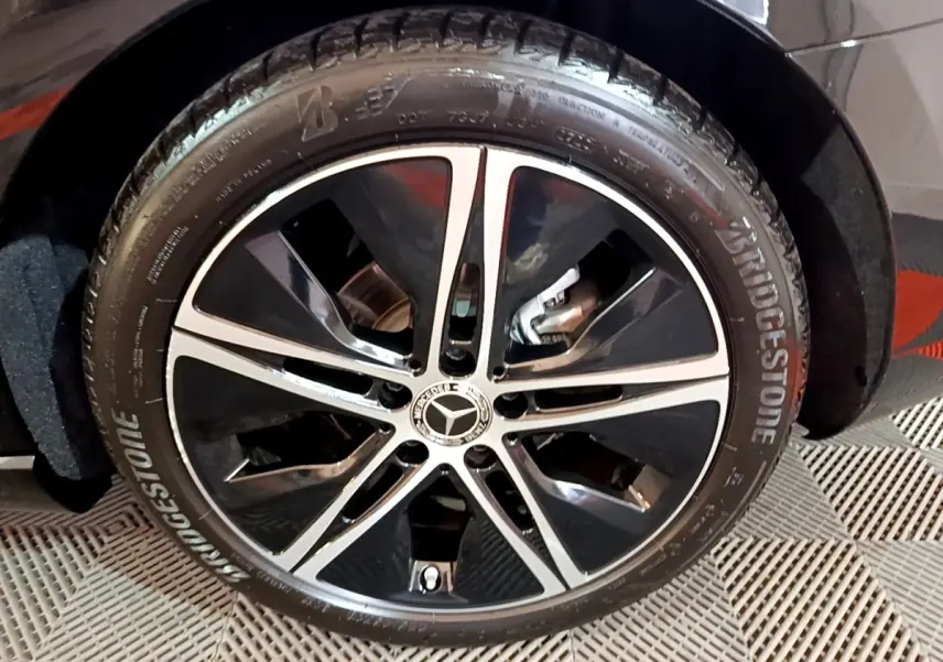 Gros plan sur la roue avant droite noire avec jante alliage bicolore et logo Mercedes visible sur une Classe A Berline noire.