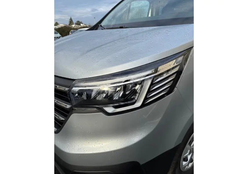 Gros plan sur l'avant droit gris clair du Renault Trafic Fourgon 2022, mettant en valeur le phare LED et la calandre humide.