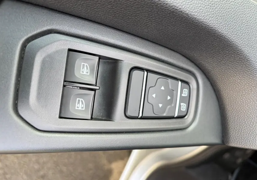 Gros plan sur les commandes de lève-vitres et réglage des rétroviseurs côté conducteur du Renault Trafic gris clair.