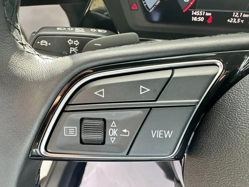 Gros plan sur les commandes multifonctions du volant cuir noir de l'Audi A3 Sportback 30 TFSI blanc Arkona, version 2024.