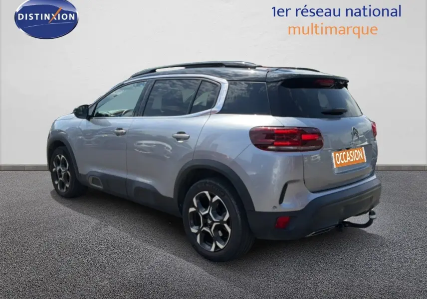 Vue 3/4 arrière droite d'un Citroën C5 Aircross gris acier avec toit noir et jantes bi-ton, stationné devant un mur blanc.
