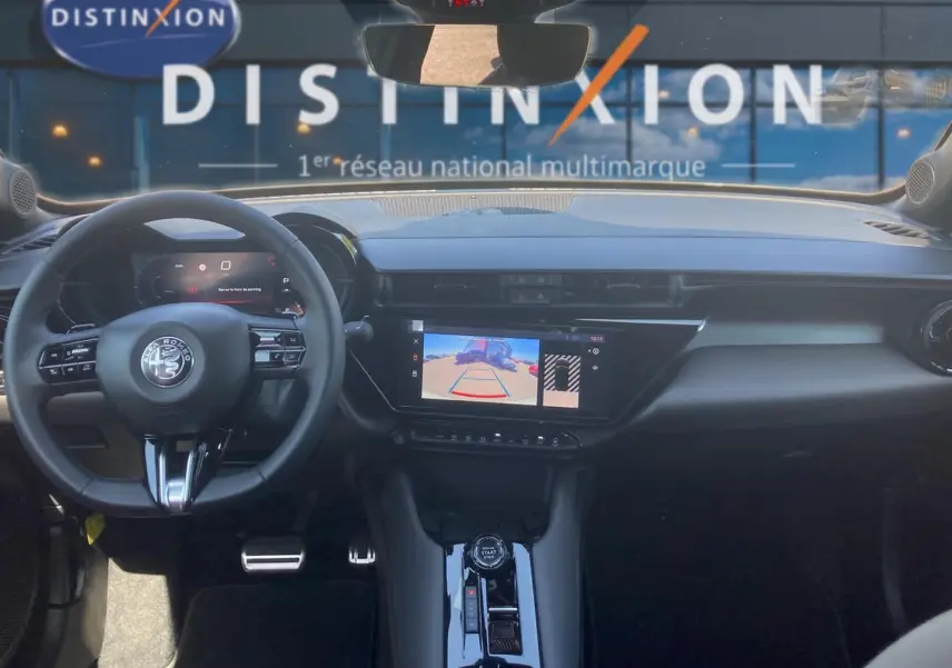 Vue intérieure avant de l'Alfa Romeo Junior 1.2 hybride, avec tableau de bord noir et écran tactile affichant la caméra de recul.