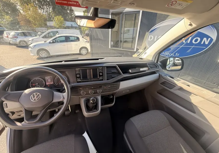 Vue intérieure avant du Volkswagen Transporter gris clair 2022, tableau de bord avec écran tactile et volant manuel.