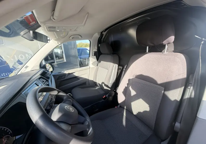 Vue intérieure côté conducteur du Volkswagen Transporter gris clair 2022, montrant le volant et les sièges avant en tissu.