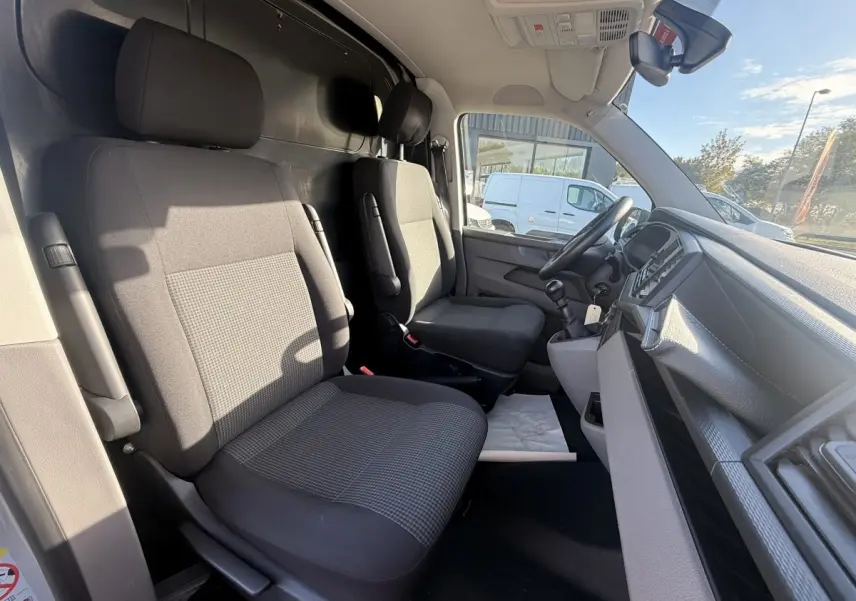 Vue intérieure côté conducteur du Volkswagen Transporter gris clair 2022, montrant les sièges avant et le tableau de bord.