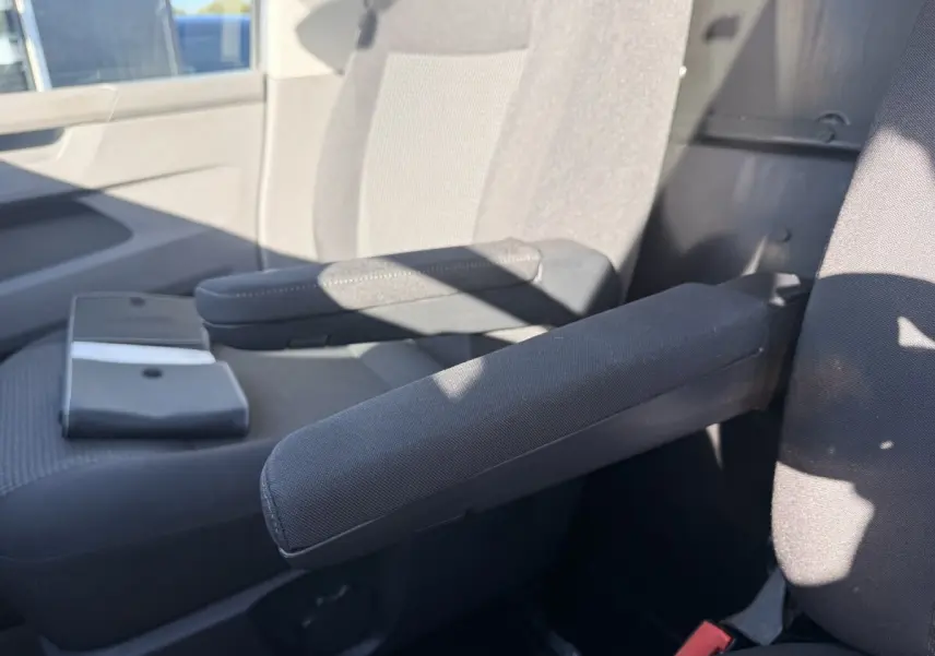 Gros plan sur les accoudoirs noirs des sièges avant d’un Volkswagen Transporter gris clair, intérieur lumineux.