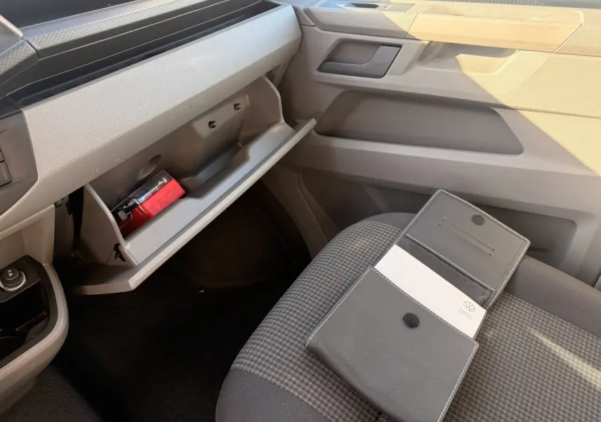 Vue intérieure côté passager du Volkswagen Transporter gris clair 2022, boîte à gants ouverte et pochette sur siège tissu gris.