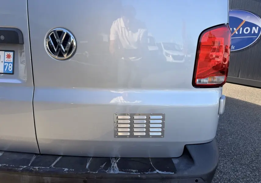 Vue arrière droite du Volkswagen Transporter gris clair avec feu arrière rouge et logo VW visible sur la porte.
